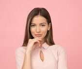 Portrait of a young woman posing elegantly in a studio with a pink background.